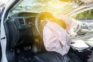 From the view of someone standing beside an open driver's side door: the driver's frontal airbag and the passenger frontal airbag have deployed and deflated. The windshield has shattered. The passenger front door is open.