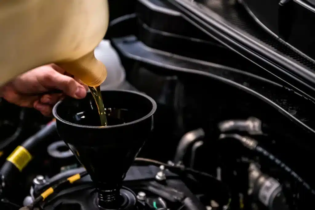 Close up of mechanic adding oil to vehicle by a funnel