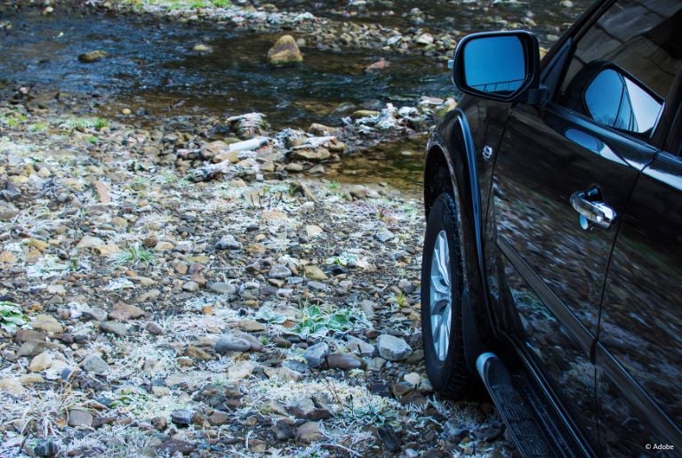 A black Ford Expedition is parked on a rocky riverbank.