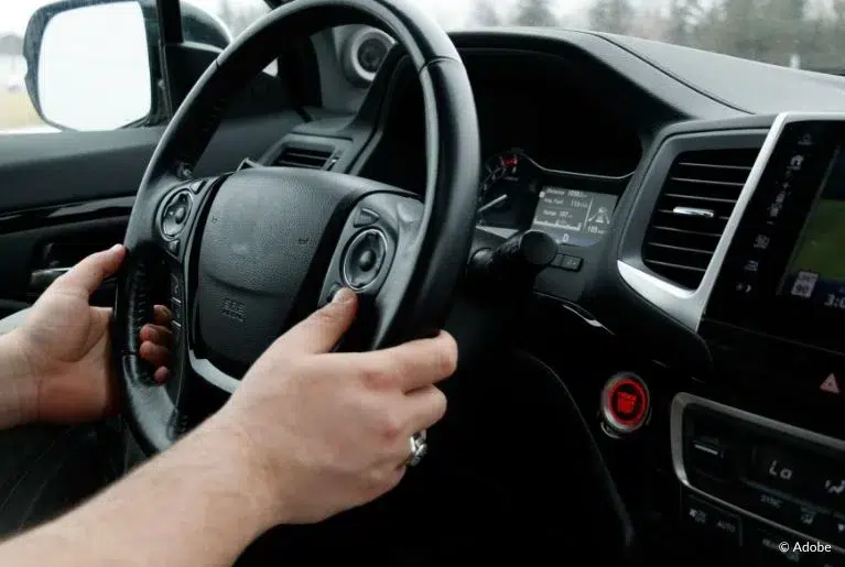 A driver holds a steering wheel. Only the driver's hands are visible.