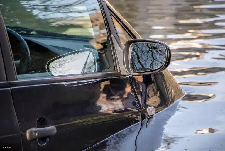 A black car is partially submerged in the floodwaters.