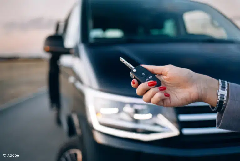 A woman holds a key fob while standing in front of a Honda vehicle. The vehicle itself is fuzzy and out of focus.