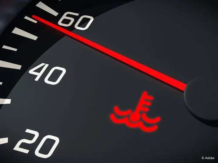 A close-up of a Coolant light illuminated on a speedometer. The speedometer indicates a speed of around 55 miles per hour.