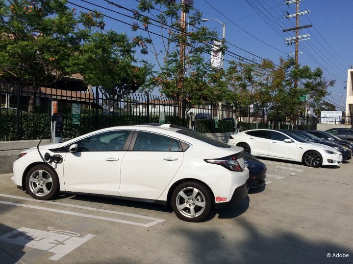 A white electrical vehicle is parked in a charging station of an outdoor parking lot.