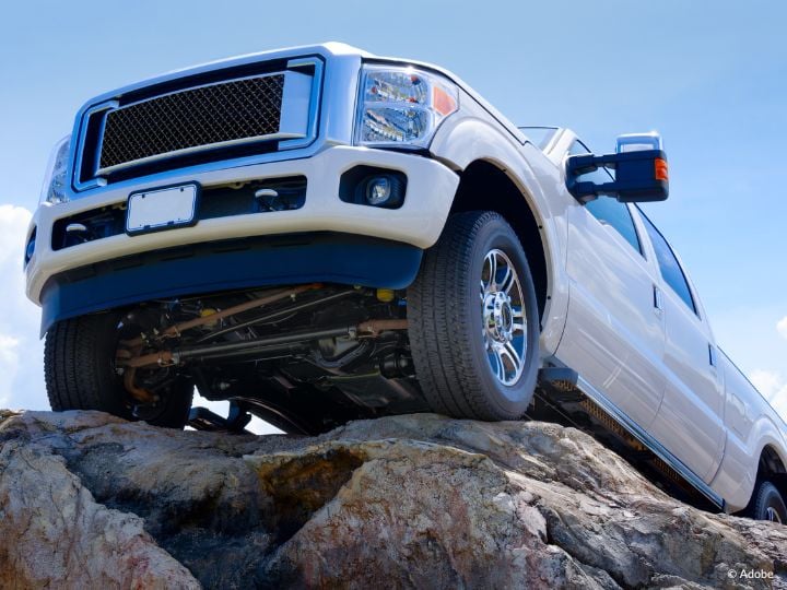 A white pickup truck is parked near the end of a rock (or a cliff). The truck has no license plate information.