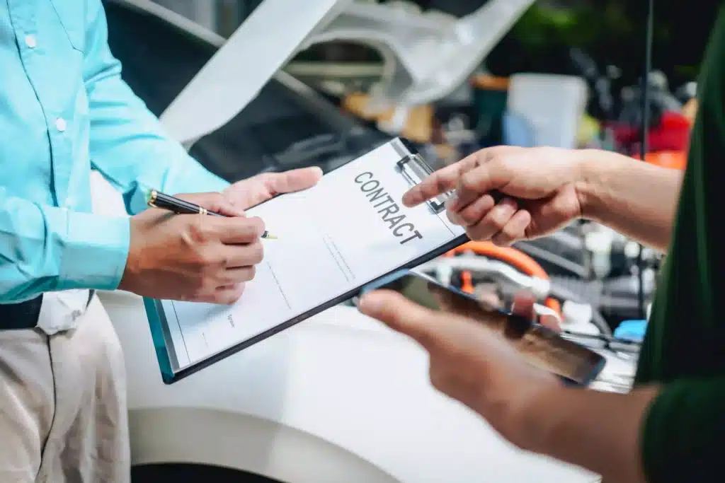 Client engaging with mechanic in repair shop with clipboard holding contract paperwork