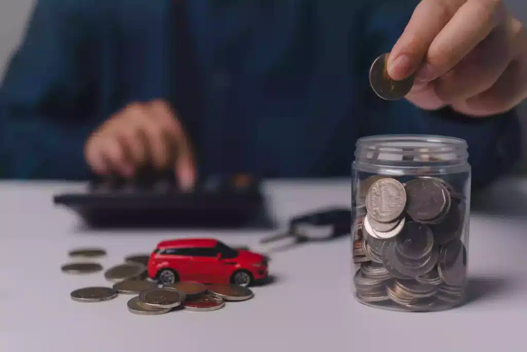 Close up of hands putting money in a jar with a vehicle next to it