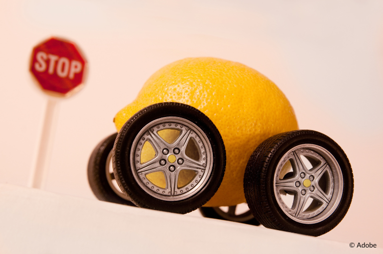 A toy car with the body of a lemon is in front of a red stop sign.