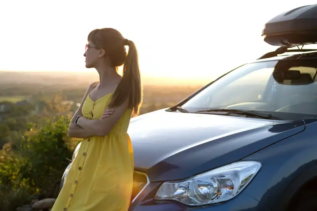 Woman leaning against hood of car admiring sunset