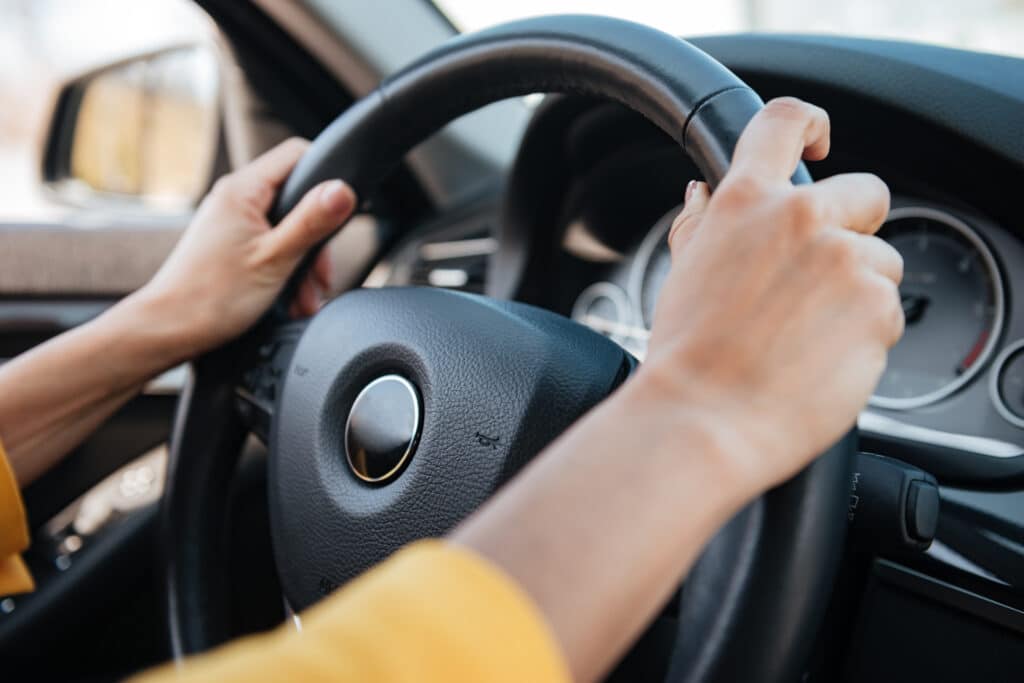 Close-up of female hands on steering wheel while driving a car.