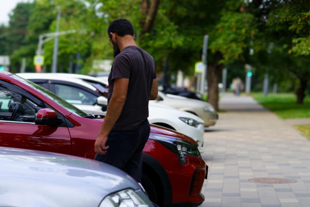 A man walks beside a parked red SUV in a parking lot.