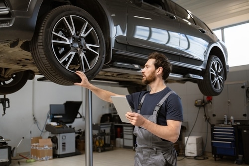 Mechanic holding tablet while inspecting raised vehicle wheel in auto repair shop
